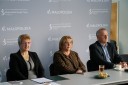 Trzy osoby siedzące przy stole konferencyjnym. Za nimi w tle ścianka z materiału z logotypami Małopolski i Wojewódzkiego Urzędu Pracy w Krakowie.