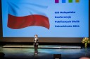 Kobieta na scenie stoi przed mikrofonem. Za nią w tle ekran z flagą Polski i napisem 13 Małopolska Konferencja Publicznych Służb Zatrudnienia 2024