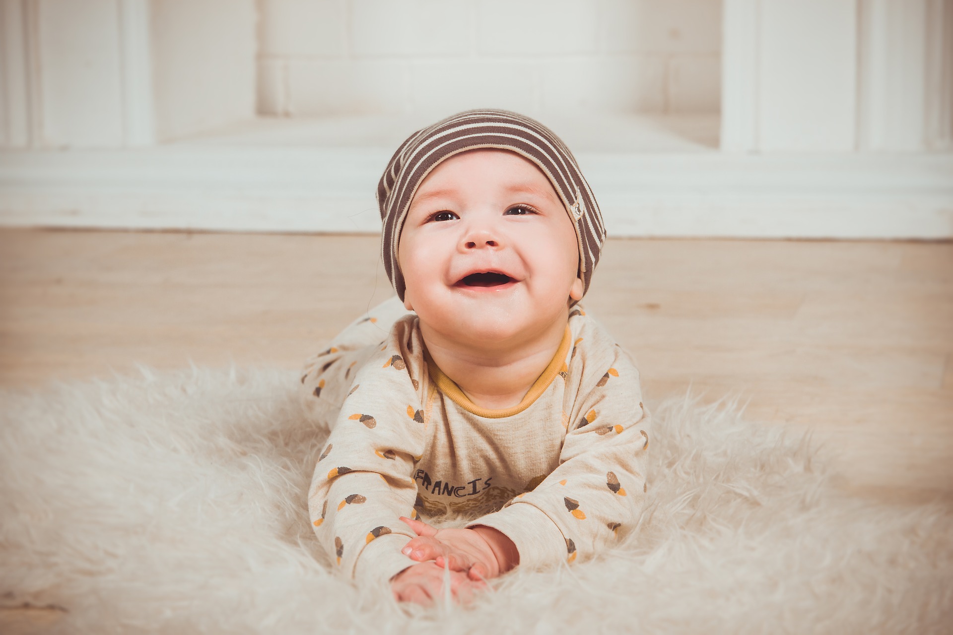 Zdjęcie przedstawiające małe, uśmiechające się dziecko leżące na dywanie